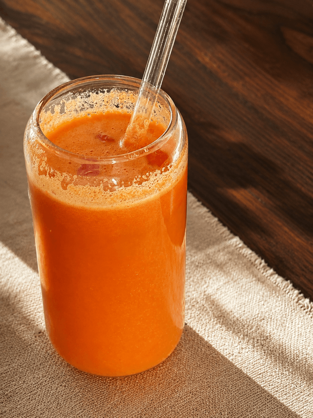 Glass of fresh orange juice with visible pulp and a straw, placed on a light textured cloth over a wooden surface