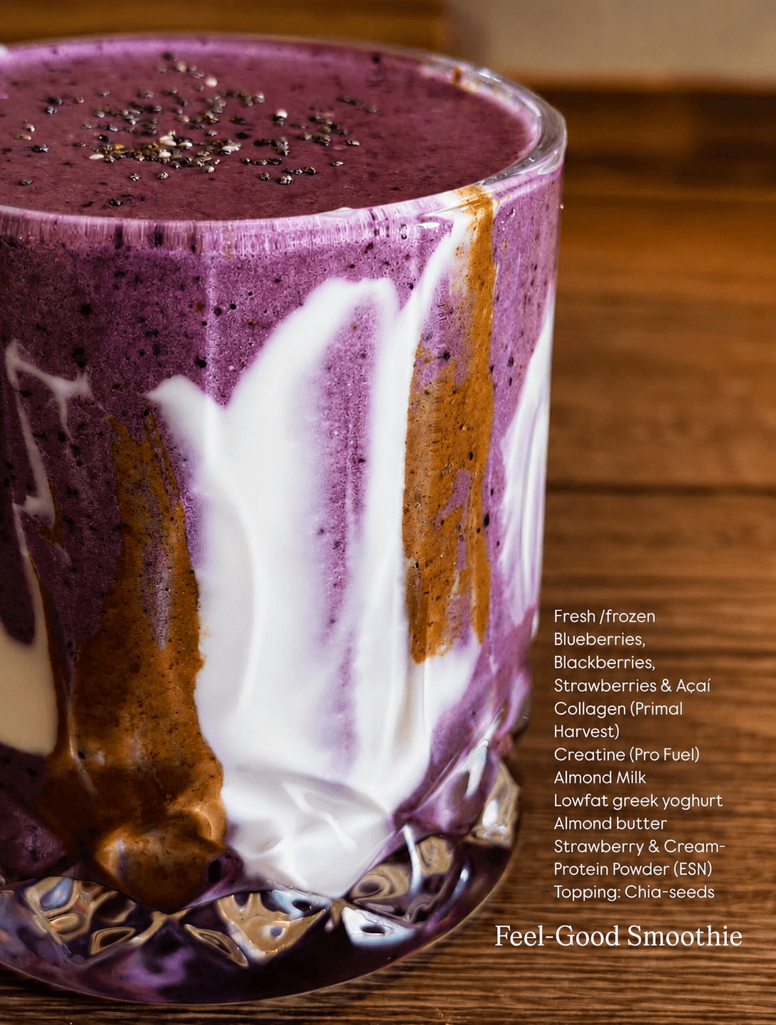 Close-up of a layered purple smoothie with visible streaks of white yoghurt and almond butter inside a glass, topped with chia seeds, placed on a wooden surface.